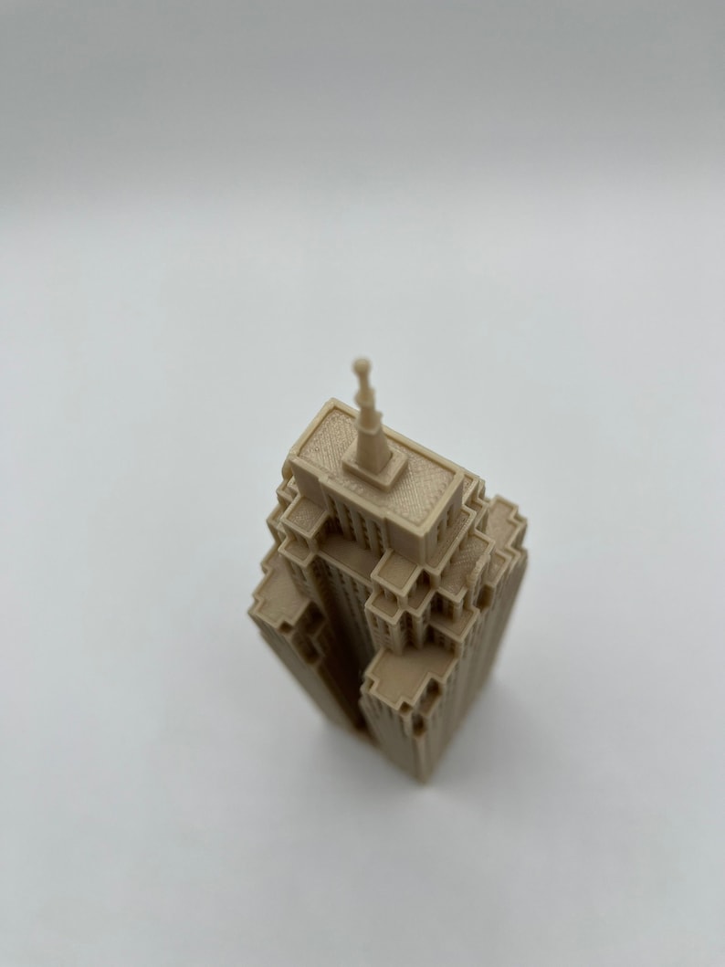 May include: A beige 3D printed model of a skyscraper with a pointed roof.