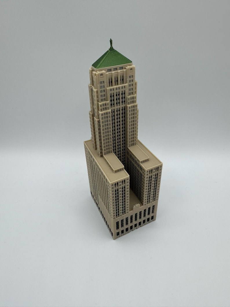 May include: A miniature beige skyscraper model with a green roof. The building has many windows and architectural details. The model is a detailed representation of a tall building.