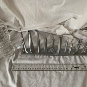 May include: A collection of silver-colored miniature skyscraper models displayed on a gray base. A clear plastic water bottle and a ruler are also in the image. The ruler measures up to 12 inches.