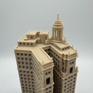Op de afbeelding: Een beige 3D-geprint model van een hoog gebouw met een koepelvormig dak en veel ramen.