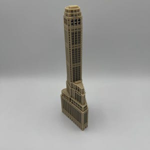 Op de afbeelding: Een beige 3D-geprint model van een hoog wolkenkrabbergebouw met een gedetailleerde gevel.