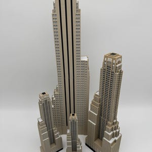 May include: A collection of beige miniature skyscraper models of varying heights. The tallest model has black vertical stripes. A wooden ruler with inch measurements is at the bottom of the image.