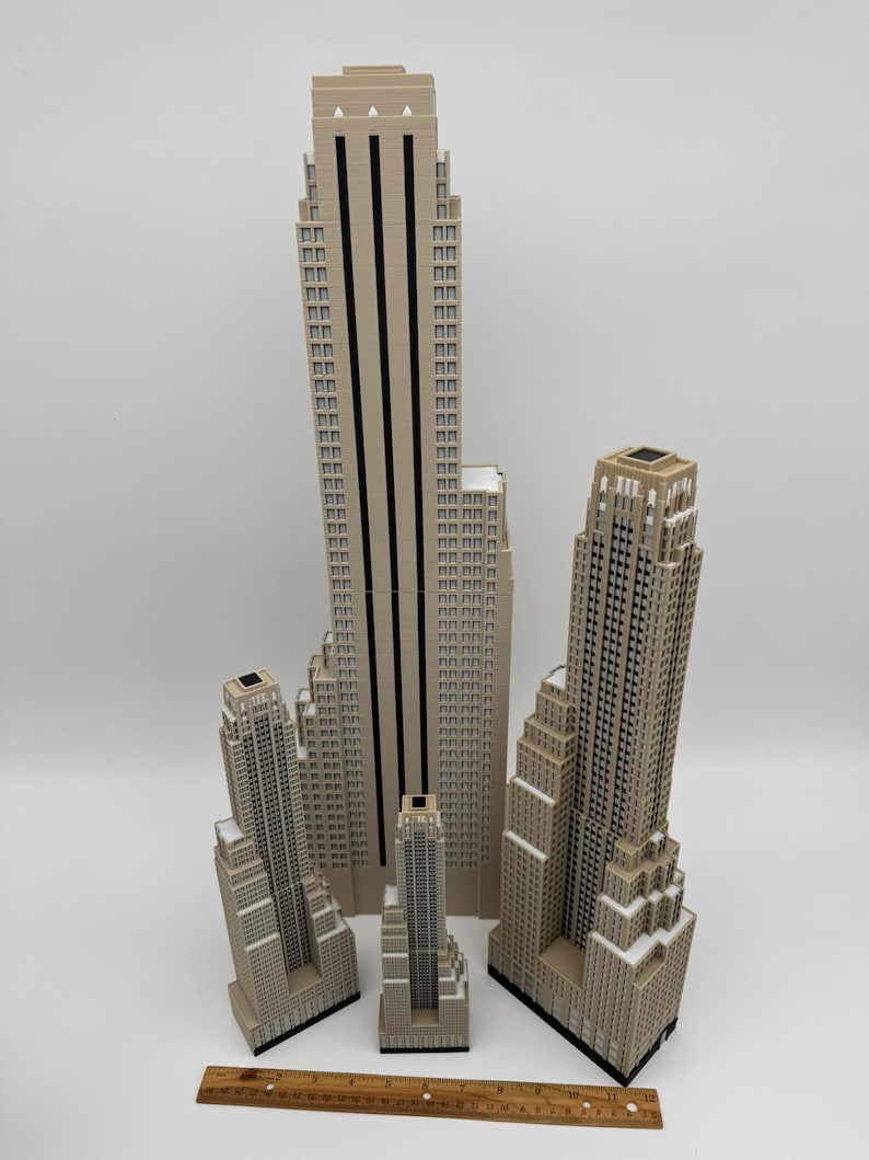 May include: A collection of beige miniature skyscraper models of varying heights. The tallest model has black vertical stripes. A wooden ruler with inch measurements is at the bottom of the image.