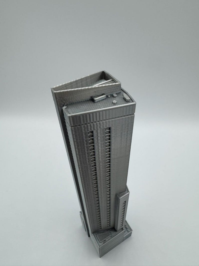 May include: A gray, 3D-printed model of a skyscraper. The building has a rectangular shape with many windows and a flat roof. The model is detailed, showing the texture of the building's facade and roof.