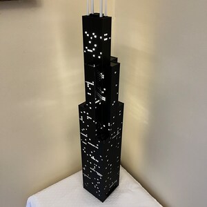 May include: A black and white model of a skyscraper with white antenna on top. The model is sitting on a white surface with a ruler in the foreground.