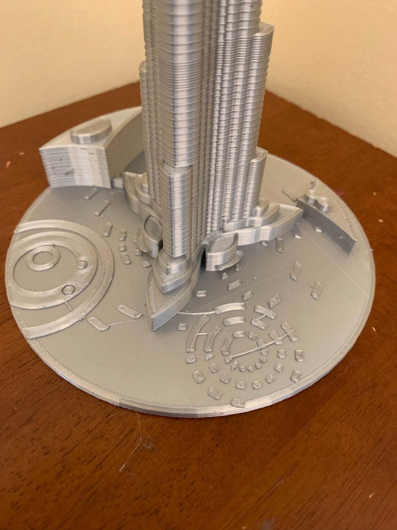 May include: A silver 3D printed model of a skyscraper with a detailed base.