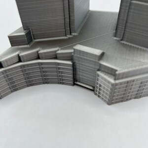 Op de afbeelding: Een 3D-geprint model van een gebouw met een gebogen gevel en een plat dak. Het model is gemaakt van grijs plastic en heeft een gedetailleerd ontwerp.