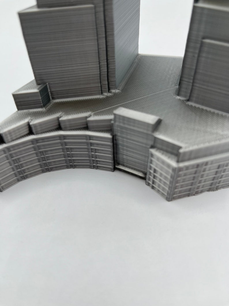 Op de afbeelding: Een 3D-geprint model van een gebouw met een gebogen gevel en een plat dak. Het model is gemaakt van grijs plastic en heeft een gedetailleerd ontwerp.