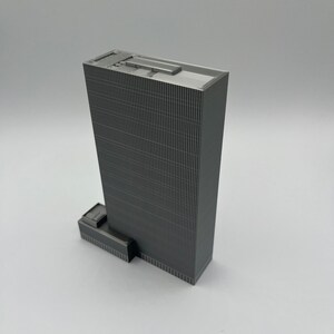 May include: A gray, detailed model of a skyscraper with a flat roof and a small, rectangular addition on the side.