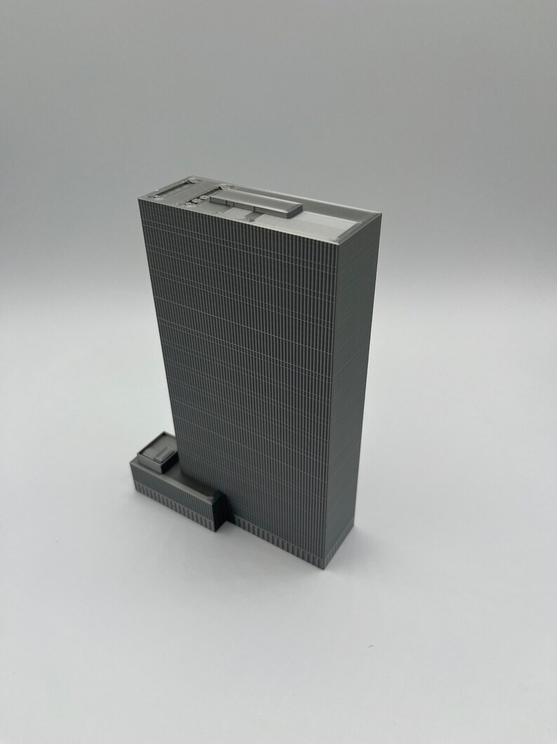 May include: A gray, detailed model of a skyscraper with a flat roof and a small, rectangular addition on the side.