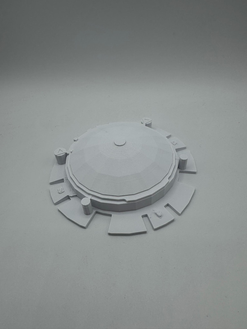 May include: A light gray, 3D-printed architectural model featuring a domed roof and a circular base with rectangular extensions. The model has a detailed, geometric design and is likely a miniature representation of a building or structure.