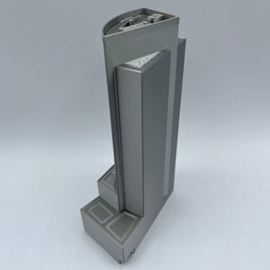 May include: A gray 3D printed model of a tall building with a flat roof and a stepped base.