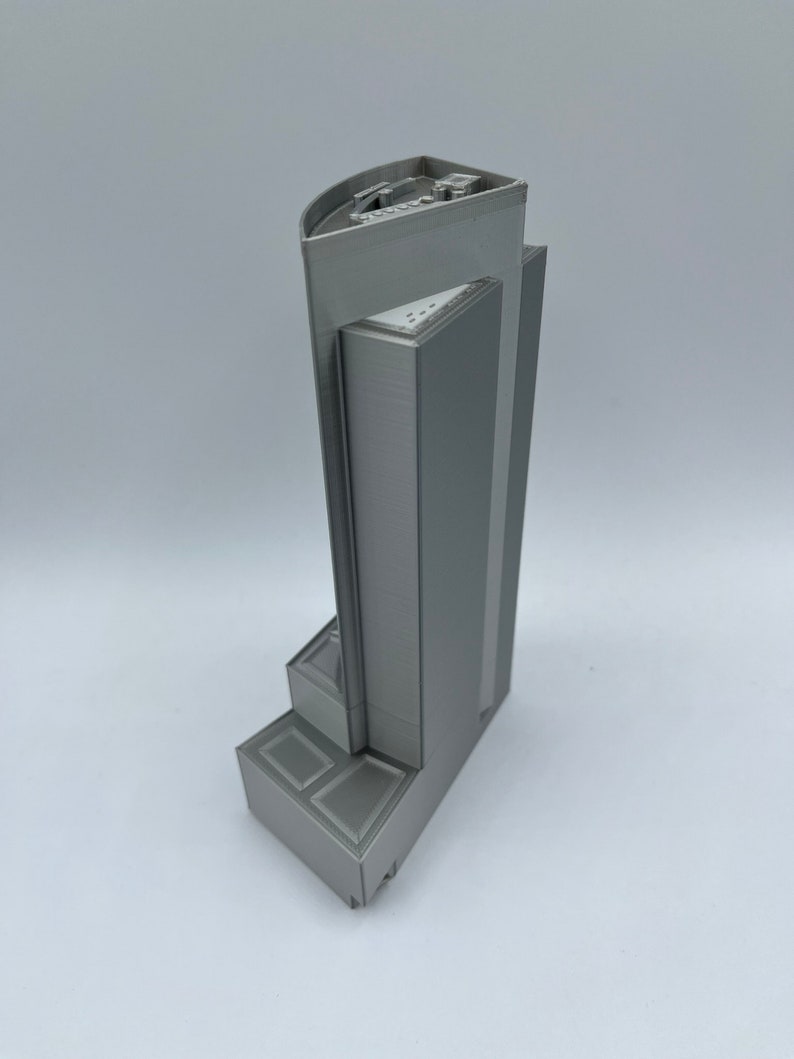 May include: A gray 3D printed model of a tall building with a flat roof and a stepped base.