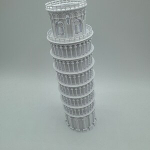 May include: A white 3D printed model of the Leaning Tower of Pisa. The model is detailed with arches, columns, and a railing at the top.