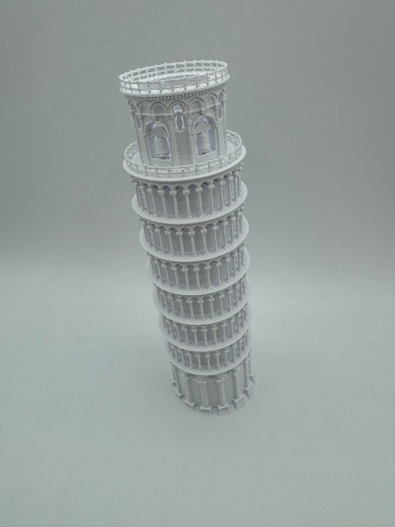 May include: A white 3D printed model of the Leaning Tower of Pisa. The model is detailed with arches, columns, and a railing at the top.