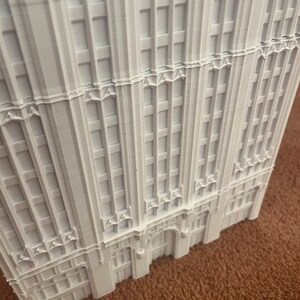 May include: A white 3D printed model of a tall building with a detailed facade. The building has many windows and a decorative entrance.