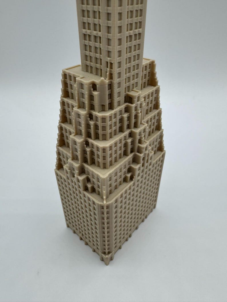May include: A beige, 3D-printed model of a skyscraper. The building has a stepped design with numerous windows and architectural details. The model is a detailed representation of a classic building.