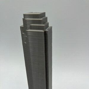 May include: A gray 3D printed model of a skyscraper with a layered design.