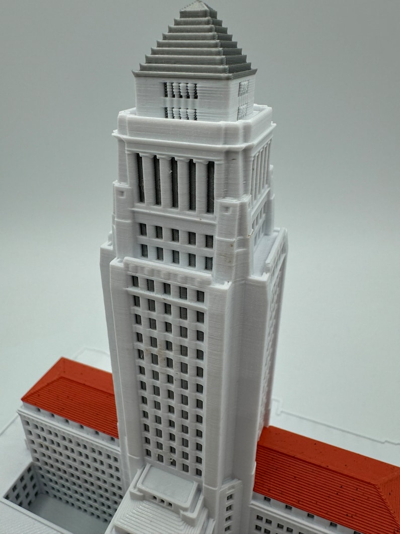 May include: A white 3D printed model of a tall building with a red roof. The building has many windows and a pointed roof.