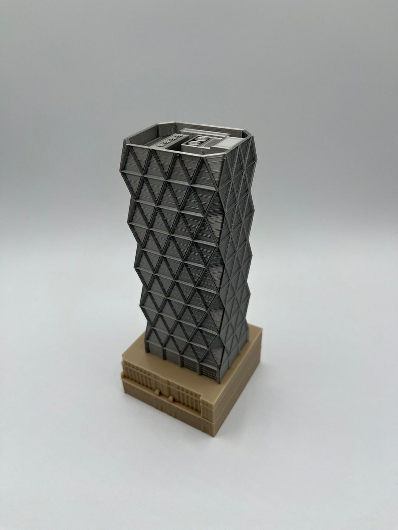 May include: A 3D printed model of a modern skyscraper with a geometric facade. The building is made of light grey plastic and has a base made of light brown plastic.