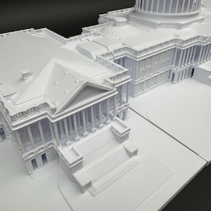 K&ouml;nnte beinhalten: Ein detailliertes, wei&szlig;es Architekturmodell des US-Kapitolgeb&auml;udes. Das Modell zeigt die ikonische Kuppel, die S&auml;ulen und die aufwendige Fassade des Geb&auml;udes und f&auml;ngt die Essenz der Struktur in Miniaturform ein.