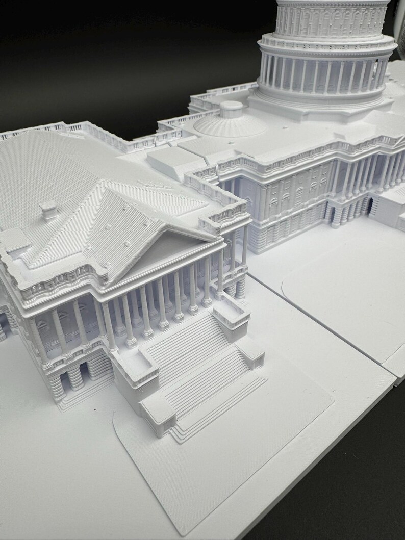 K&ouml;nnte beinhalten: Ein detailliertes, wei&szlig;es Architekturmodell des US-Kapitolgeb&auml;udes. Das Modell zeigt die ikonische Kuppel, die S&auml;ulen und die aufwendige Fassade des Geb&auml;udes und f&auml;ngt die Essenz der Struktur in Miniaturform ein.