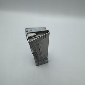 May include: A gray, 3D-printed miniature skyscraper model. The building has a rectangular base and a tall, multi-story design with detailed architectural features. The model is made of a solid, matte gray material.