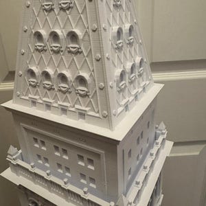 Op de afbeelding: Een wit 3D-geprint model van een hoog gebouw met een gedetailleerde toren en meerdere ramen.