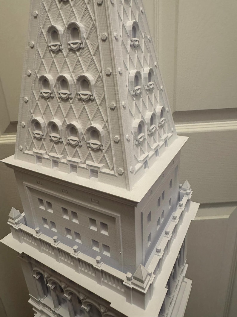 Op de afbeelding: Een wit 3D-geprint model van een hoog gebouw met een gedetailleerde toren en meerdere ramen.