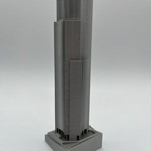 May include: A gray 3D printed model of a skyscraper with a square base.