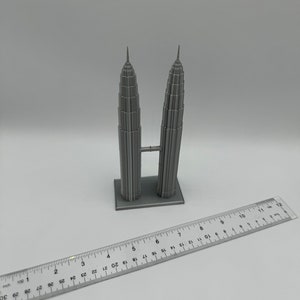 May include: A gray 3D printed model of the Petronas Towers, a famous landmark in Kuala Lumpur, Malaysia. The model is approximately 6 inches tall and is sitting on a white surface.