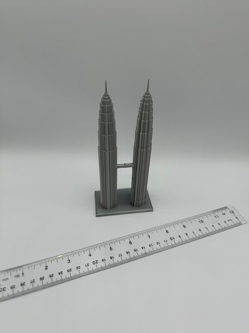 May include: A gray 3D printed model of the Petronas Towers, a famous landmark in Kuala Lumpur, Malaysia. The model is approximately 6 inches tall and is sitting on a white surface.