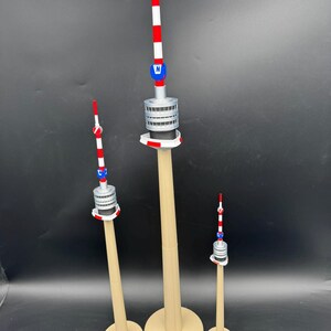 Op de afbeelding: Drie miniatuur torenmodellen met beige bases en palen. De torens hebben een rood, wit en blauw gestreepte antenne, een zilveren middengedeelte en een blauw embleem. De torens vari&euml;ren in grootte, de hoogste is ongeveer 30 cm hoog.