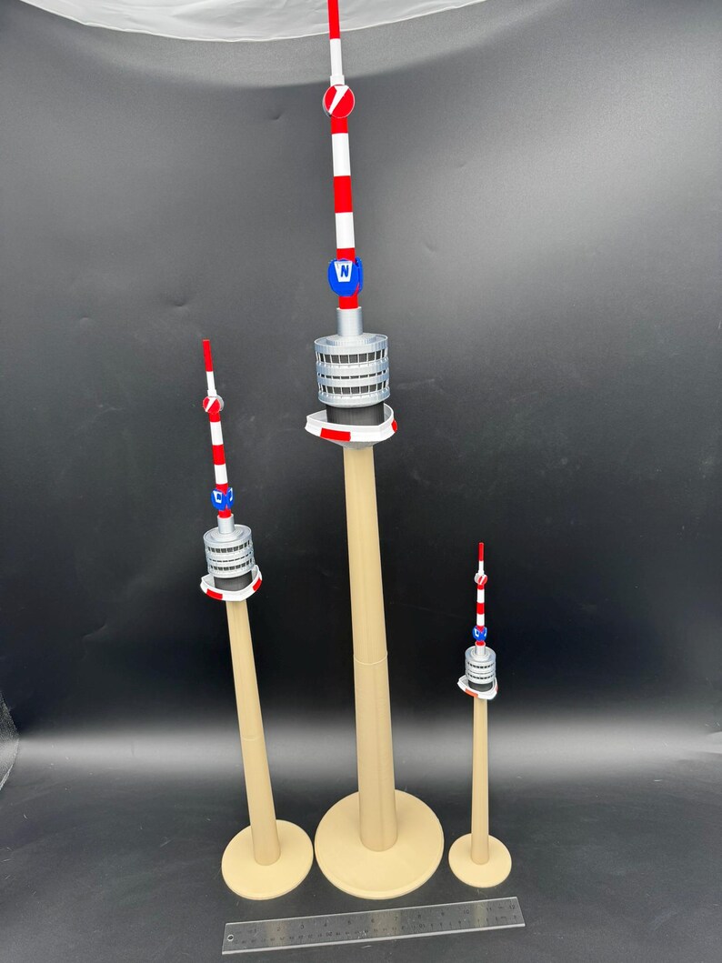 Op de afbeelding: Drie miniatuur torenmodellen met beige bases en palen. De torens hebben een rood, wit en blauw gestreepte antenne, een zilveren middengedeelte en een blauw embleem. De torens vari&euml;ren in grootte, de hoogste is ongeveer 30 cm hoog.