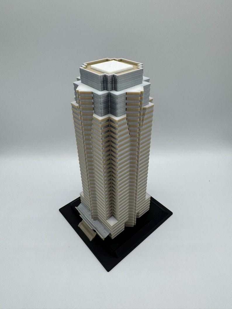 May include: A 3D-printed model of a skyscraper. The building is primarily beige with gray and white accents, and sits on a black square base. The architectural model has a detailed, geometric design.