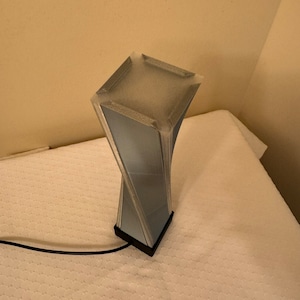 May include: A blue and black twisted lamp with a square base. The lamp is on a white surface.