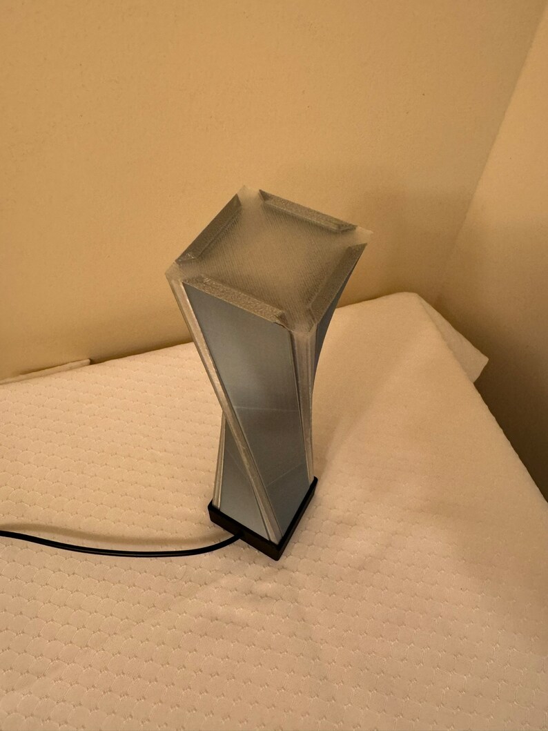 May include: A blue and black twisted lamp with a square base. The lamp is on a white surface.