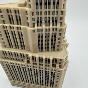Op de afbeelding: Een gedetailleerd 3D-geprint model van een hoog gebouw met veel ramen. Het model is gemaakt van lichtbeige plastic en heeft een textuur.