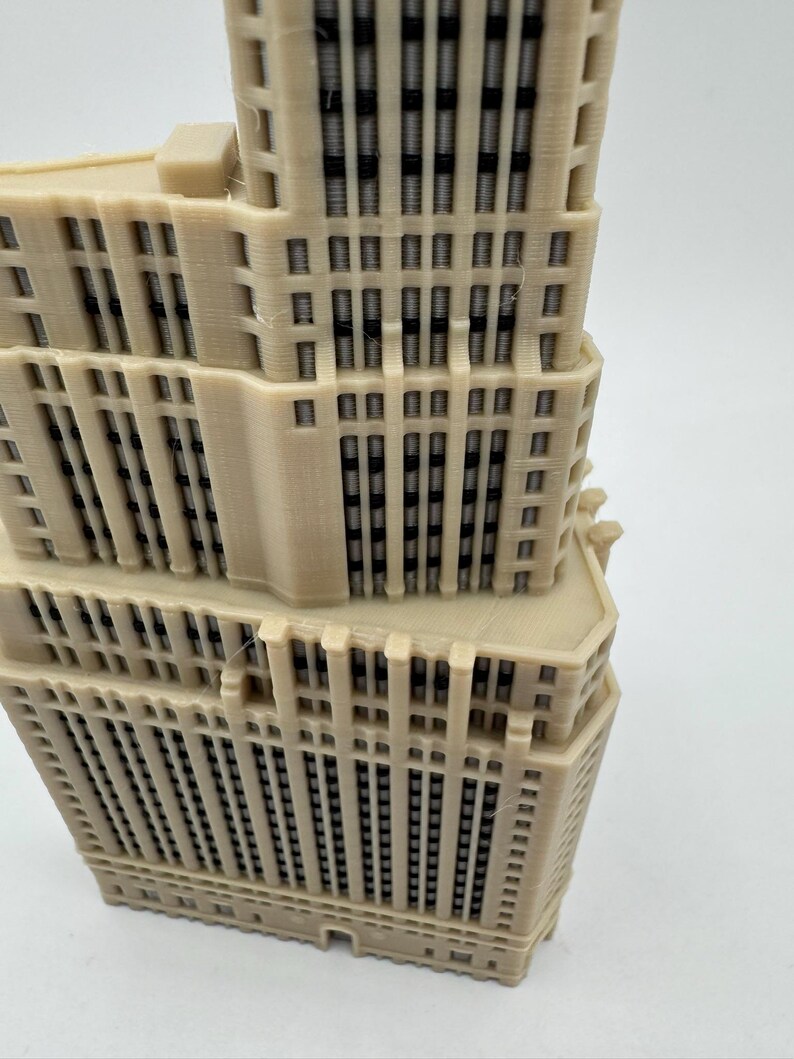 Op de afbeelding: Een gedetailleerd 3D-geprint model van een hoog gebouw met veel ramen. Het model is gemaakt van lichtbeige plastic en heeft een textuur.