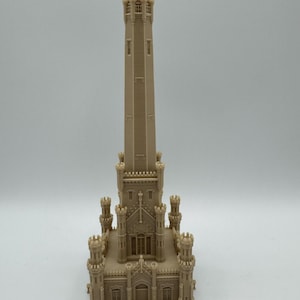 May include: A beige architectural model of a tall tower with intricate details, including turrets, windows, and a domed top. The model is a detailed replica of a historic building, showcasing its architectural features.