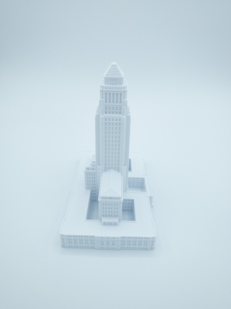 May include: A white 3D printed model of a city hall building with a tall tower and a square base.