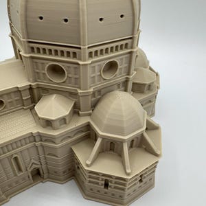 May include: A beige 3D-printed model of the Florence Cathedral, featuring a large dome with multiple circular openings and detailed architectural elements. The model showcases the building's intricate design and structure.