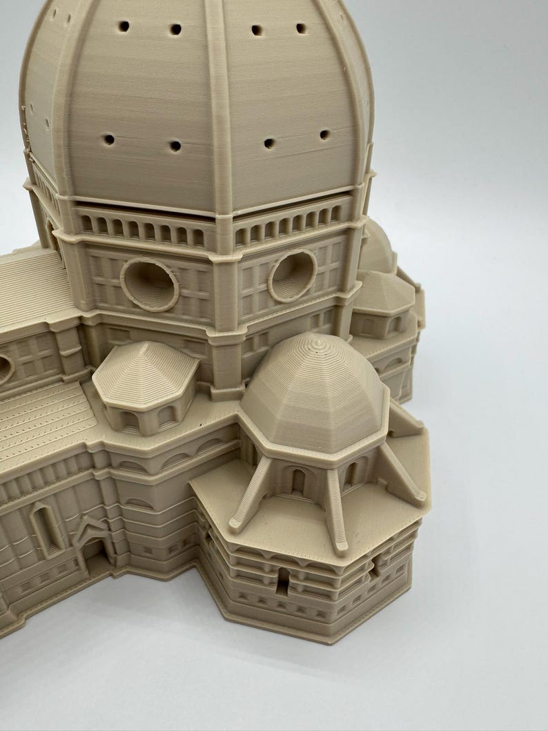 May include: A beige 3D-printed model of the Florence Cathedral, featuring a large dome with multiple circular openings and detailed architectural elements. The model showcases the building's intricate design and structure.