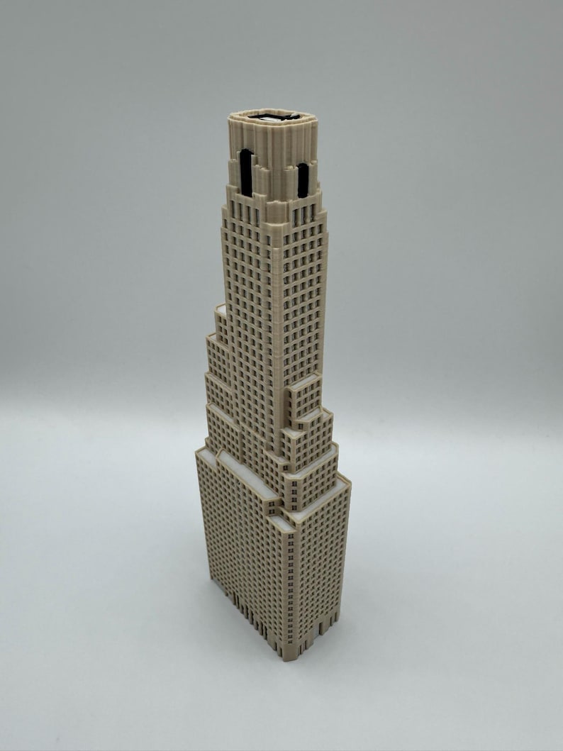 May include: A beige 3D printed architectural model of a skyscraper featuring a stepped design with multiple levels, a grid of small square windows, and a flat roof section. The structure has a vertical orientation with a central tower section.