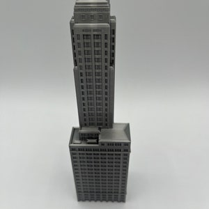 May include: A gray 3D printed model of a tall skyscraper building with a flat roof and many windows.