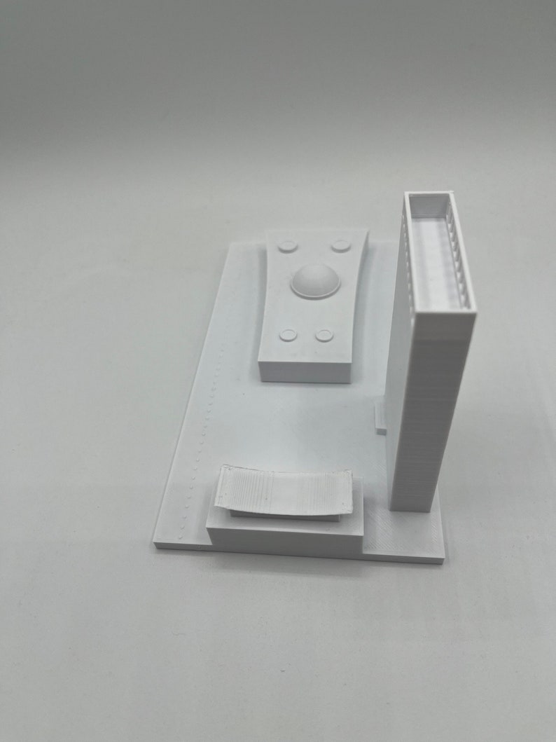 K&ouml;nnte beinhalten: Wei&szlig;es 3D-gedrucktes Modell eines Geb&auml;udes mit einem Kuppeldach, einem rechteckigen Geb&auml;ude mit einem Balkon und einer geschwungenen Bank. Das Modell steht auf einem wei&szlig;en Sockel.