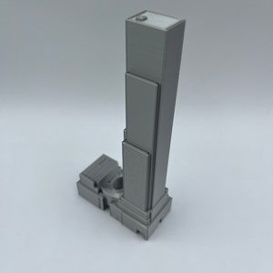 May include: A gray 3D printed model of a skyscraper with a flat roof and multiple windows.