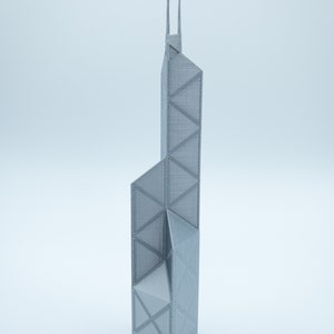 May include: A gray, 3D-printed model of a tall skyscraper with a geometric design. The building has a rectangular base and a series of triangular and trapezoidal shapes. Two vertical spires extend from the top.