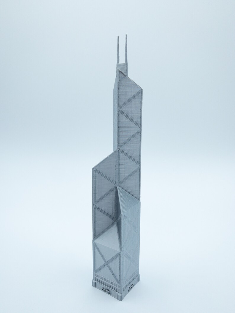May include: A gray, 3D-printed model of a tall skyscraper with a geometric design. The building has a rectangular base and a series of triangular and trapezoidal shapes. Two vertical spires extend from the top.