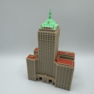 May include: A detailed model of a tall building with a light brown facade, red roof accents, and a green top. The building has many windows and architectural details, resembling a skyscraper.